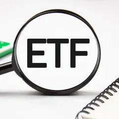 Magnifying glass focuses on "ETF" text, hinting at stock analysis. A calculator and notebook are nearby.