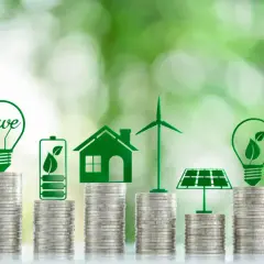 Stacks of coins topped with green icons of a lightbulb, battery, house, wind turbine, and solar panel, illustrating how to invest in renewable energy.