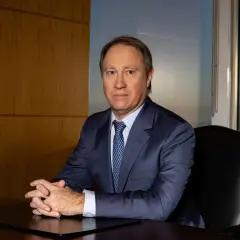 A man in a suit sits at a desk, hands clasped, in an office with a city view. He looks like he's discussing important Morgan Stanley acquisitions.