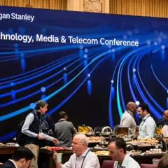 Attendees mingle at a Morgan Stanley TMT conference, with a large screen displaying the event title and a blue, abstract network graphic.