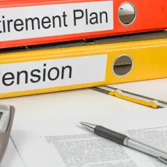 Two binders labeled "Retirement Plan" and "Pension" sit on a desk with a calculator and pen, ready for financial planning.