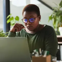 A woman with glasses intently studies her laptop, perhaps researching alternative investment partners for her next venture.