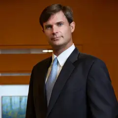 Dennis Lynch, a distinguished professional at Morgan Stanley, poses confidently in a dark suit and light blue patterned tie.