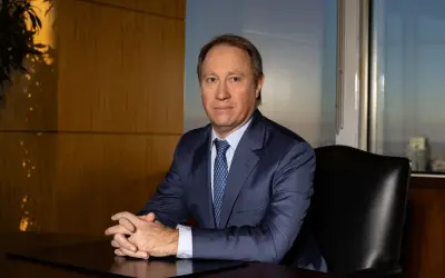 A man in a suit sits at a desk, hands clasped, in an office with a city view. He looks like he's discussing important Morgan Stanley acquisitions.