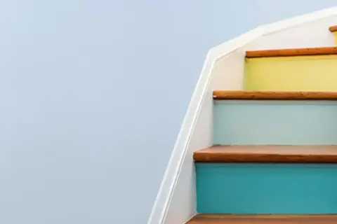 A young girl sits on colorful stairs, engrossed in a tablet, a bright future made possible by a Morgan Stanley 529 plan.