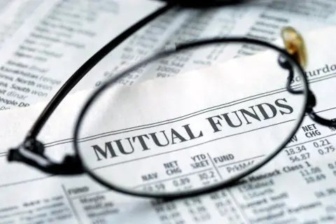 Glasses focus on "MUTUAL FUNDS" in a financial newspaper, hinting at investment research for a vanguard star fund.