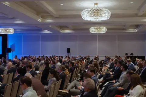 Attendees at the Morgan Stanley Laguna Conference listen intently in a large ballroom with ornate chandeliers.
