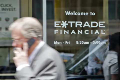 A man on the phone walks past a window displaying "Welcome to E*TRADE FINANCIAL." This image captures the moment before the Morgan Stanley E*TRADE acquisition.