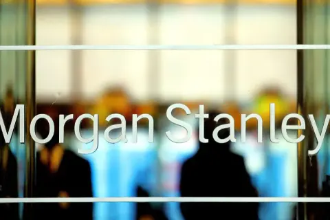 Glass doors with "Morgan Stanley" etched in white letters. Blurred figures are visible inside, suggesting a busy office environment.