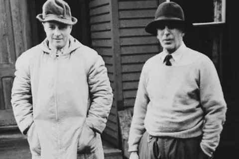 Two men in hats, one in a long coat, the other in a sweater, possibly representing the early days of Morgan Stanley founder.
