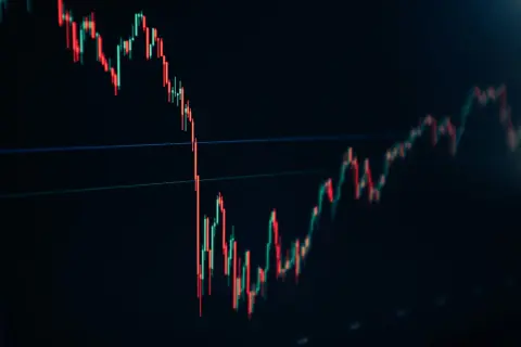 A stock trading chart shows red and green candlesticks on a dark background, indicating market fluctuations.