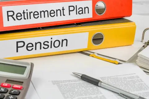 Two binders labeled "Retirement Plan" and "Pension" sit on a desk with a calculator and pen, ready for financial planning.