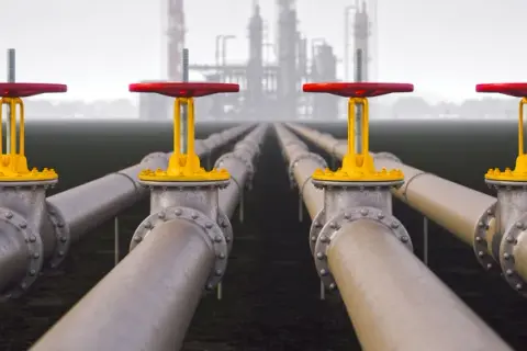 Rows of industrial pipes with red and yellow valves stretch towards a hazy refinery, symbolizing Morgan Stanley infrastructure.
