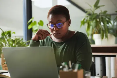 A woman with glasses intently studies her laptop, perhaps researching alternative investment partners for her next venture.