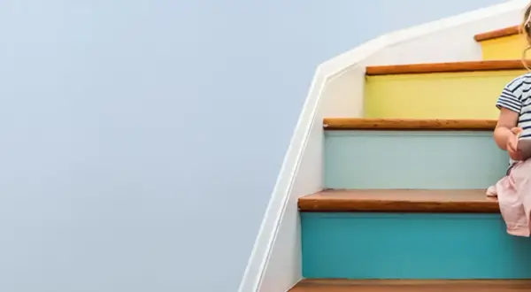 A young girl sits on colorful stairs, engrossed in a tablet, a bright future made possible by a Morgan Stanley 529 plan.
