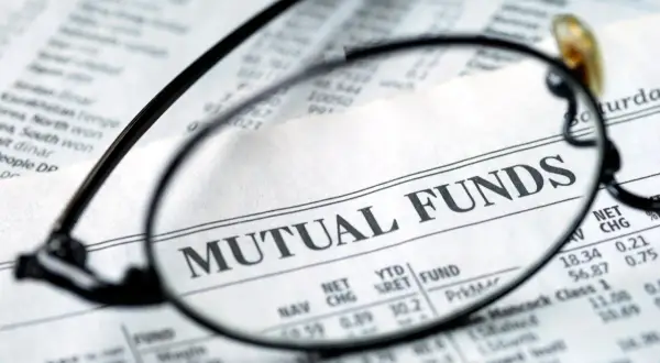Glasses focus on "MUTUAL FUNDS" in a financial newspaper, hinting at investment research for a vanguard star fund.