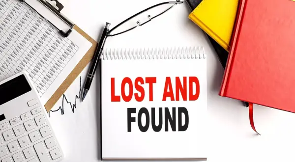 Searching for lost 401k accounts? This image shows a desk with financial documents, a calculator, and a notebook with "LOST AND FOUND" written on it, suggesting a search for forgotten assets.