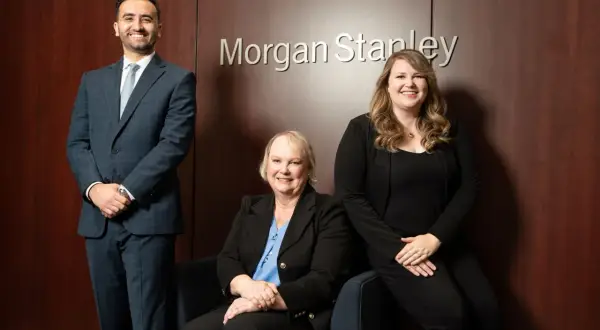 Three professionals, including Monica Guerra, pose in front of the Morgan Stanley logo.