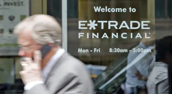 A man on the phone walks past a window displaying "Welcome to E*TRADE FINANCIAL." This image captures the moment before the Morgan Stanley E*TRADE acquisition.