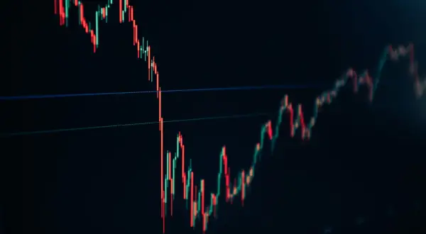A stock trading chart shows red and green candlesticks on a dark background, indicating market fluctuations.