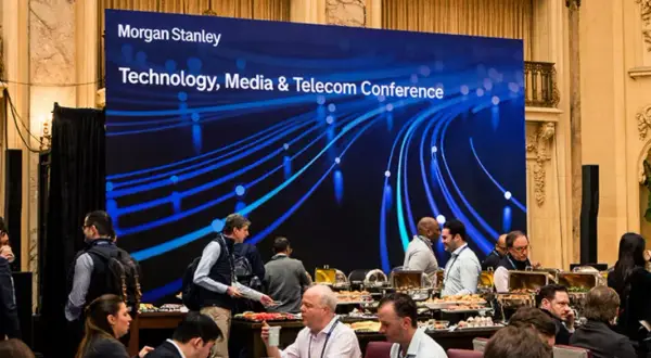 Attendees mingle at a Morgan Stanley TMT conference, with a large screen displaying the event title and a blue, abstract network graphic.