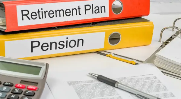 Two binders labeled "Retirement Plan" and "Pension" sit on a desk with a calculator and pen, ready for financial planning.