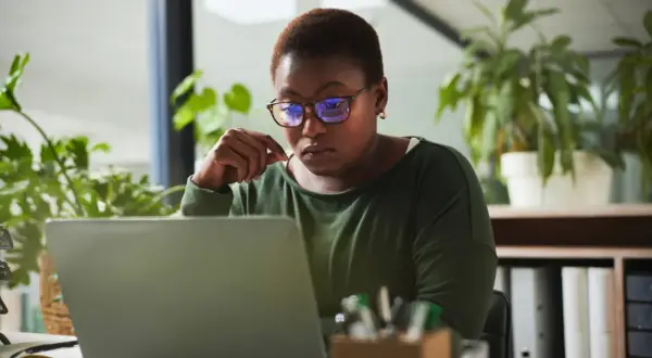 A woman with glasses intently studies her laptop, perhaps researching alternative investment partners for her next venture.