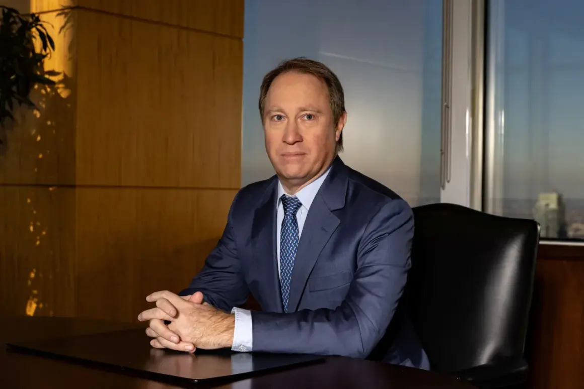 A man in a suit sits at a desk, hands clasped, in an office with a city view. He looks like he's discussing important Morgan Stanley acquisitions.