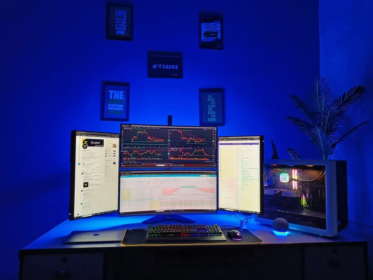 A multi-monitor setup for day trading for beginners, with charts and data displayed. Inspirational quotes about trading adorn the blue-lit wall.