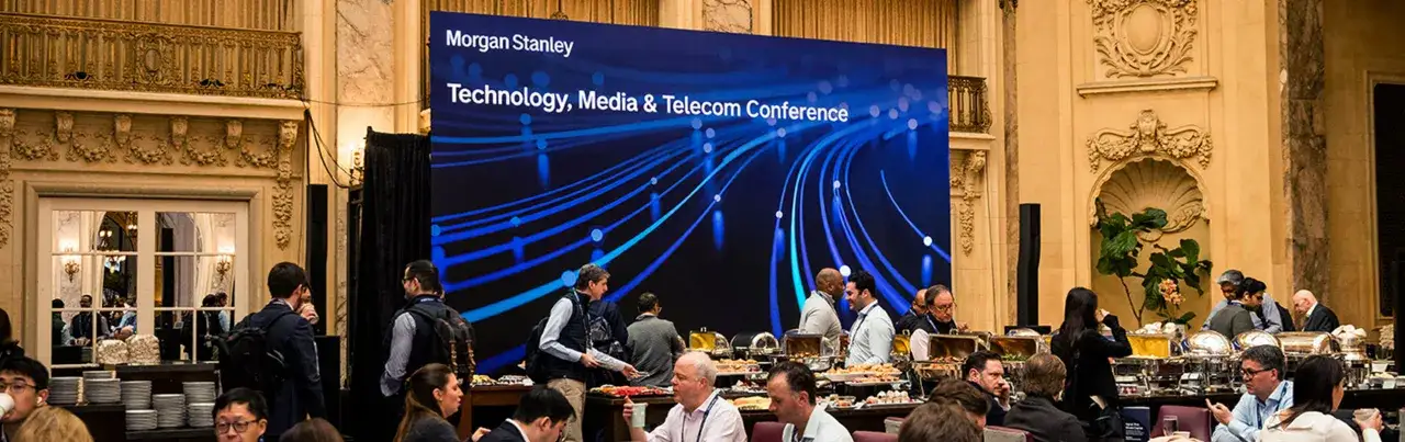 Attendees gather at a buffet during the Morgan Stanley Technology, Media & Telecom Conference, with a large screen displaying the event's branding.