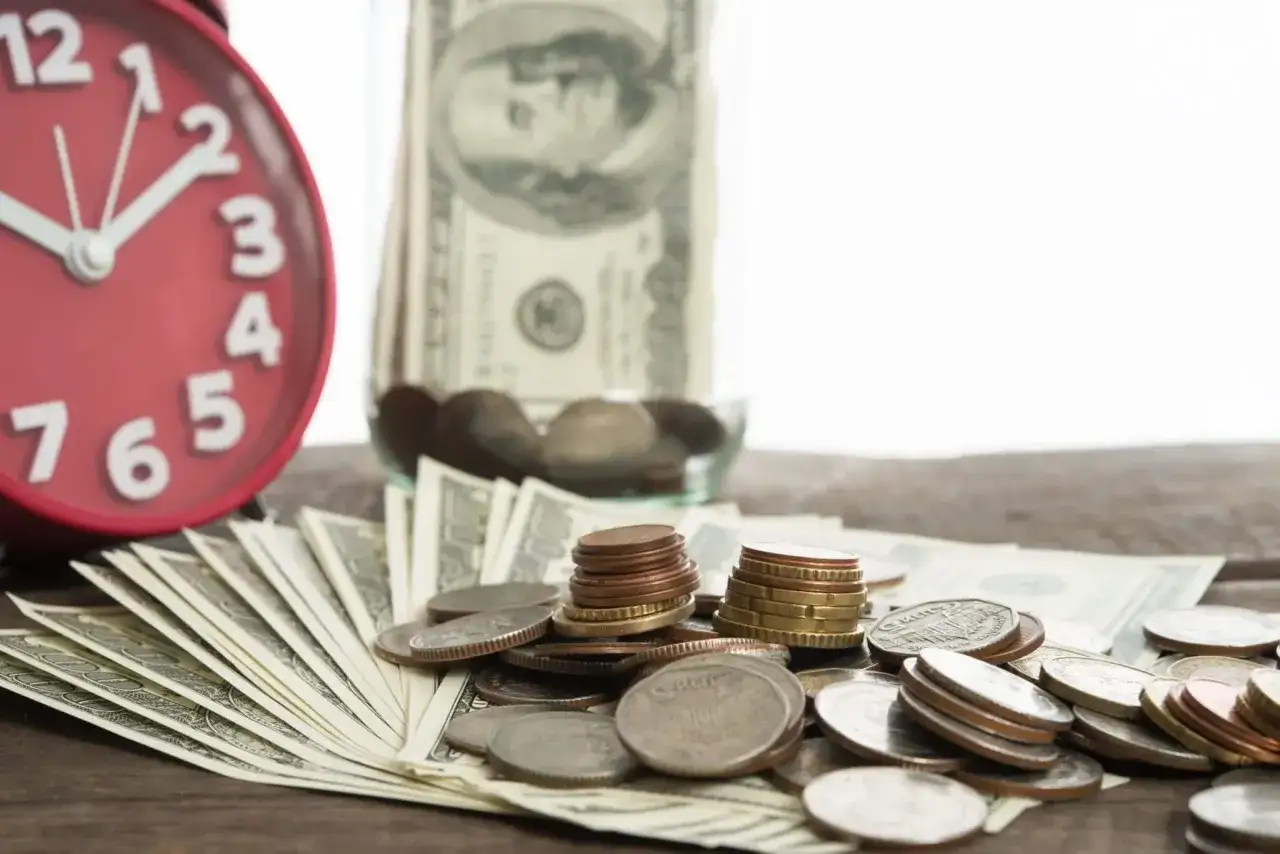 A red alarm clock and scattered coins and bills suggest it's time to find old 401k accounts.
