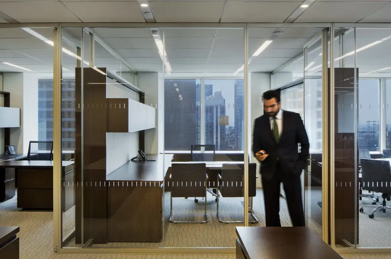 A blurred businessman, Alan Thomas Morgan Stanley, walks through a modern office with glass walls, holding his phone.