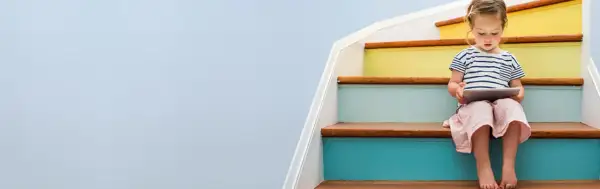 A young girl sits on colorful stairs, engrossed in a tablet, a bright future made possible by a Morgan Stanley 529 plan.