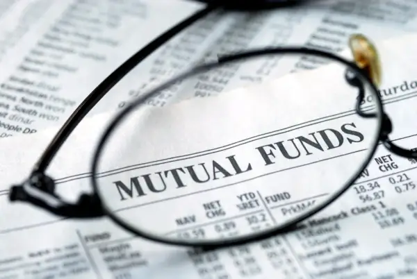 Glasses focus on "MUTUAL FUNDS" in a financial newspaper, hinting at investment research for a vanguard star fund.