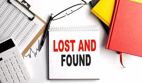 Searching for lost 401k accounts? This image shows a desk with financial documents, a calculator, and a notebook with "LOST AND FOUND" written on it, suggesting a search for forgotten assets.