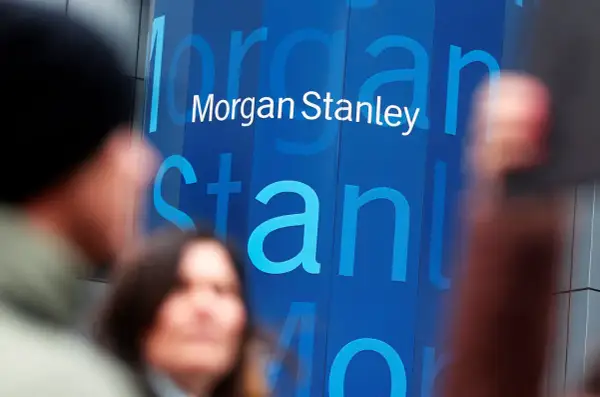 Blurred figures stand before a blue building with the "Morgan Stanley" logo. Investors anticipate the latest Morgan Stanley earnings report.
