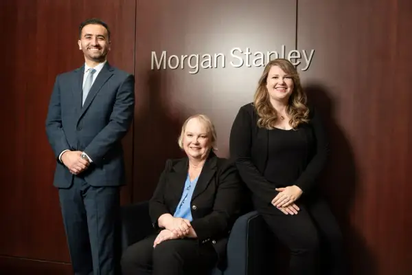 Three professionals, including Monica Guerra, pose in front of the Morgan Stanley logo.