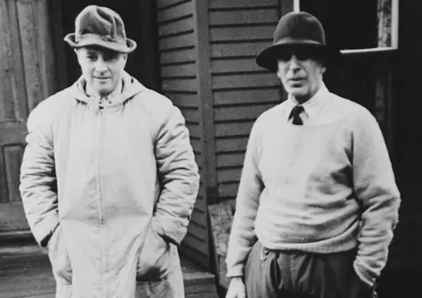 Two men in hats, one in a long coat, the other in a sweater, possibly representing the early days of Morgan Stanley founder.