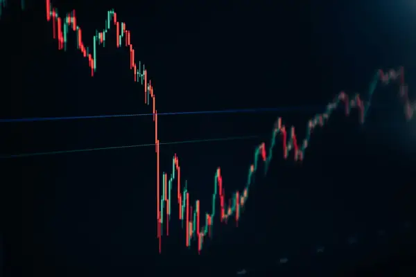 A stock trading chart shows red and green candlesticks on a dark background, indicating market fluctuations.